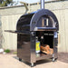 Alternate side view of the Pyro Kitchen Caldo V2 Hybrid Pizza Oven with logs, propane tank, and included accessories like the fold-up peel and log holder.