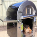 Side view of the Pyro Kitchen Caldo V2 Hybrid Pizza Oven with logs, propane tank, and 14-inch stainless steel side shelf, showcasing hybrid functionality with wood and gas compatibility.